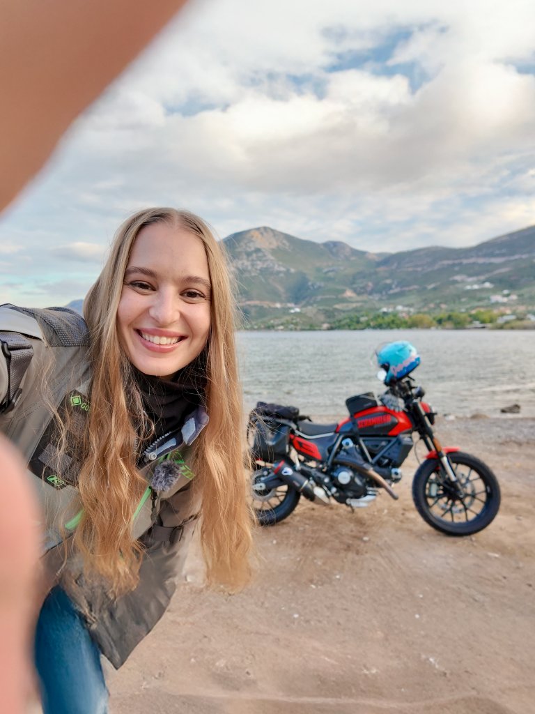 A girl taking a selfie of her and her scrambler ducati on a beach